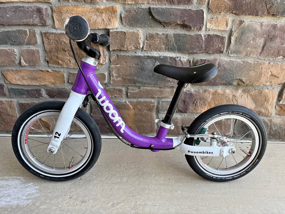 Purple Woom 1 balance bike with 12-inch wheels against a brick wall